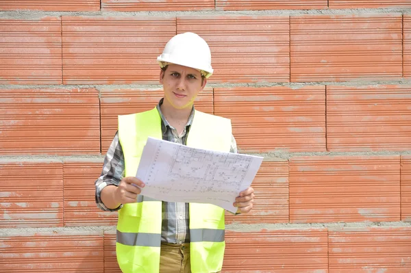 Engineer builder in front of orange brick wall with plan