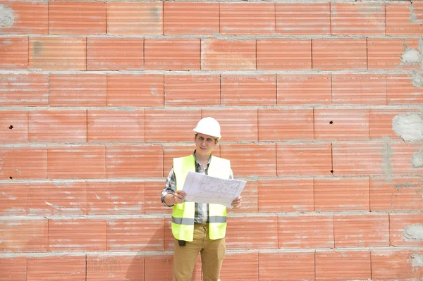 Інженер будівельник перед оранжевою цегляною стіною з планом — стокове фото