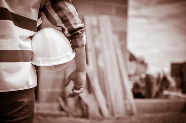 Εργαζόμενος κρατώντας ένα κράνος με το υπόβαθρο του εργοταξίου. — Φωτογραφία Αρχείου