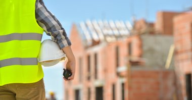 Bir kask inşaat sitenin arka planı ile holding işçi.