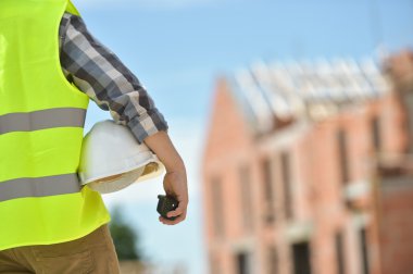 Bir kask inşaat sitenin arka planı ile holding işçi.
