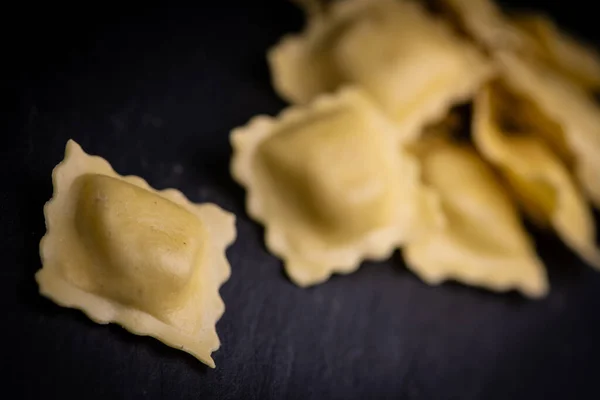 Chutné syrové ravioli s moukou a špenátem na tmavém pozadí, proces tvorby italských ravioli — Stock fotografie