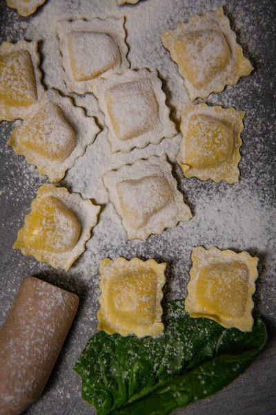 Chutné syrové ravioli s moukou a špenátem na tmavém pozadí, proces tvorby italských ravioli — Stock fotografie