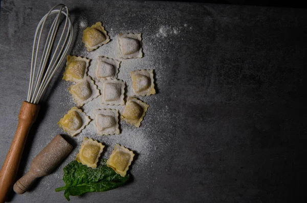 Sabrosos ravioles crudos con harina y espinacas sobre fondo oscuro, proceso de elaboración de ravioles italianos —  Fotos de Stock