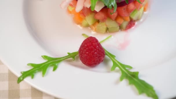 Tatarák z čerstvě nakrájené zeleniny a salátů v bílém talíři zdobený malinami — Stock video