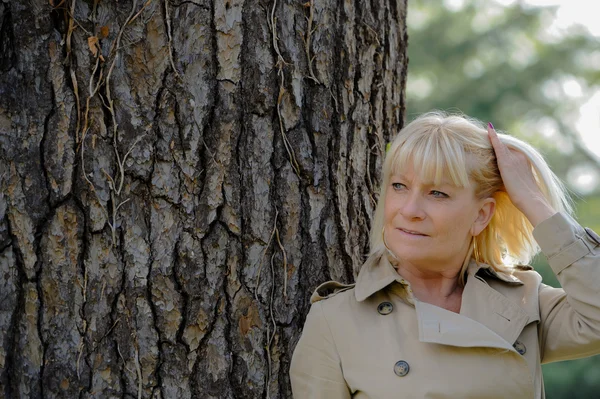 Portrait of a smiling senior woman leaning on a tree — Stock Photo, Image