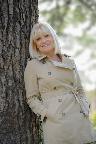 Retrato de uma mulher sênior sorridente apoiada em uma árvore — Fotografia de Stock