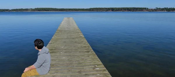 Mladý chlapec sedí na hozený jezero — Stock fotografie