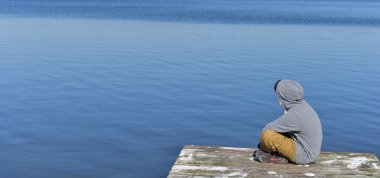 Atılmış bir göl kenarında oturan genç çocuk