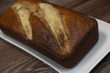 Sliced banana bread rests on a white plate, showing its rich brown color and golden crust. The sweet aroma fills the air, inviting everyone to enjoy this delicious treat.