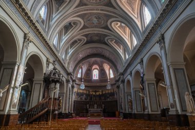 The interior of Sainte-Marie-Madeleine church features stunning architecture with intricate details, high ceilings, and decorative stained glass. The space is inviting and majestic.