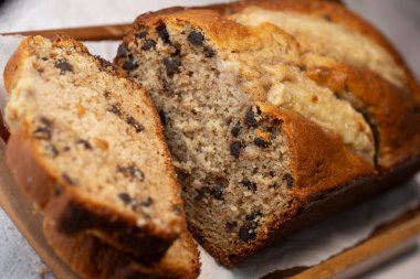 Freshly baked banana bread is sliced and displayed on a wooden cutting board. The bread has a golden-brown crust and chocolate chips, perfect for a cozy snack at home.