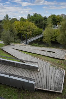 Mont de Marsan 'daki nehir kıyısındaki ahşap yol. Bereketli yeşil ağaçlar yolu çerçeveler ve açık bir günde arka planda köprüler görülebilir.