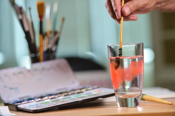 Main d'artiste nettoyant sa brosse dans un verre d'eau — Photo