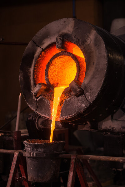 Steel worker in protective clothing raking furnace in an industr