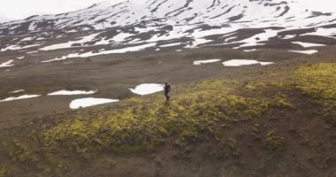 İzlanda 'nın açık arazisinde yürüyen yalnız bir yürüyüşçü, İzlanda' nın kayalık arazilerini ve karlı dağlarını gören bir hava aracı.