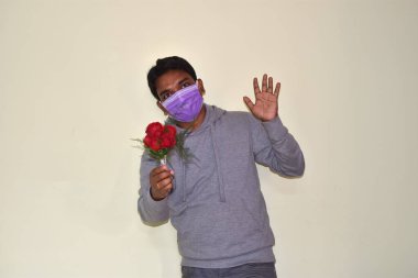 Elinde kırmızı güller ve sevgililer günü kartı olan tıbbi maske takan bir adam. Sevgililer Günü fikirleri. COVID 19 'un önlenmesi. Seçici odak.