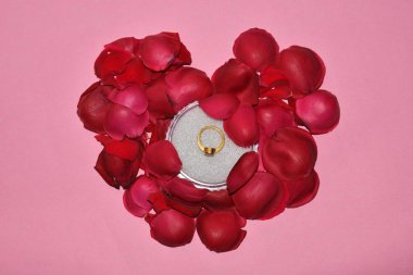 Kırmızı kalpte kırmızı gülden yapılmış yuvarlak bir kutuda altın alyans. Düğün anı, yıldönümü, nişan, ya da Sevgililer Günü.