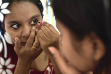 Makyaj yapan ve aynanın önüne siyah oklar çizen bir kadın..