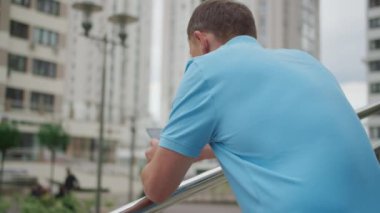 Cep telefonu olan genç adam merdivenlerde duruyor, korkulukların yanında, yan görüş, kamera hareketi.