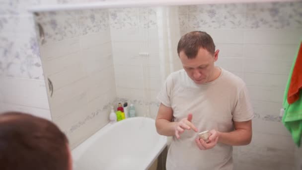 Genç adam yüzüne krem sürer, banyoda durur, cilt bakımı yapar. — Stok video