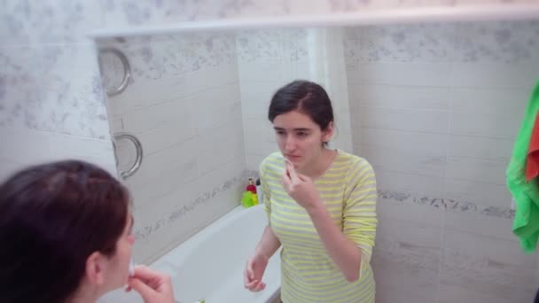 어린 소녀는 면으로 얼굴을 닦고 거울을 들여다보며 뒤를 바라본다 — 비디오