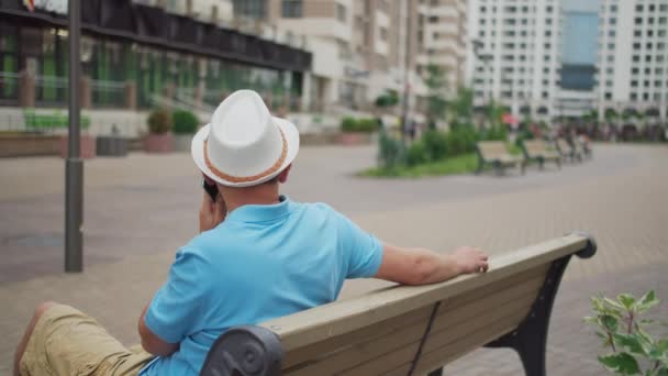 Touriste masculin dans un chapeau se repose alors qu'il est assis sur un banc, mouvement de la caméra — Video