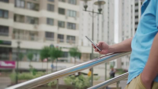 Man uses a mobile phone stands on the stairs near the railing on the background of the city, side view, camera movement — Stock Video