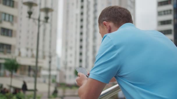 Jongeman met mobiele telefoon staat op de trap bij de reling, camerabeweging — Stockvideo