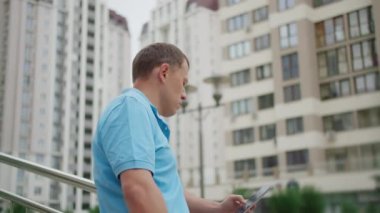 Şortlu, cep telefonu olan bir adam merdivenlerde, arka plandaki korkulukların yanında duruyor. Kamera hareketi.