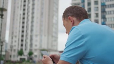 Adam merdivenlerde cep telefonu standı kullanıyor şehrin arka planındaki parmaklıklar, kamera hareketleri.