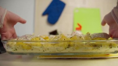 Kadın fırında yemek hazırlıyor, tavukla patates tabağı koyuyor, kamera takibi yapıyor.