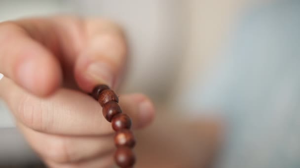 Mans hand with wooden rosary, goes through rosary, blurred background — Stock Video