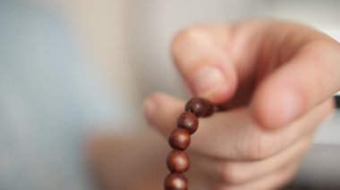 Ahşap bir tespihle bir adamın eli, bir tespihten geçer, bulanık bir arka plan, yakın plan