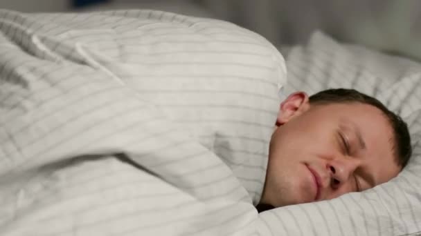 Ung man lägger sig i sängen under täcket och somnar, avslappning koncept — Stockvideo