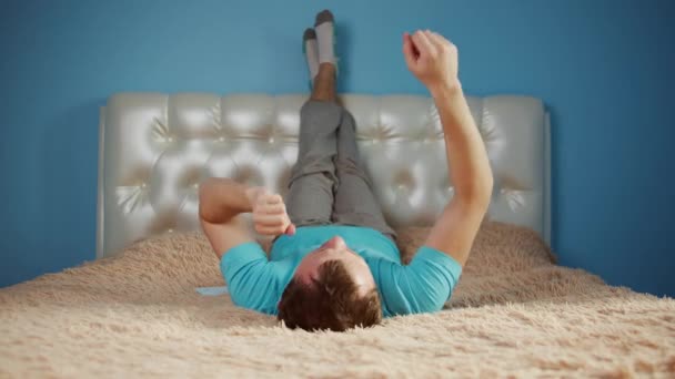 침대에 누워 재미있게 춤을 추며 다리를 들고 있는 청년 — 비디오