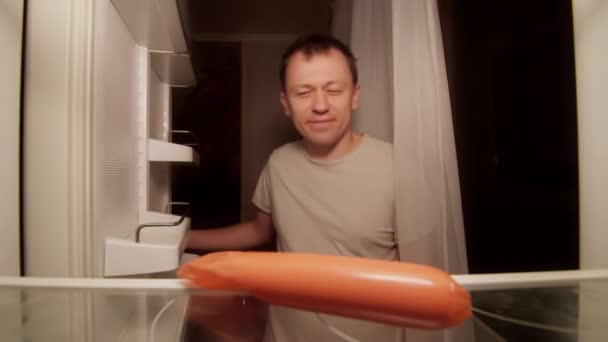 냉장고에 상한 소시지를 담고 있는 배고픈 외로운 남자 — 비디오