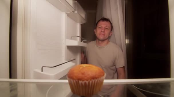 Мужчина открывает холодильник ночью на полке один кекс, недовольный человек — стоковое видео