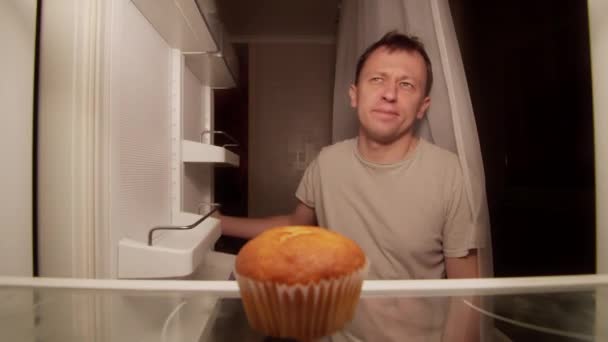 冷蔵庫にカップケーキがあり、男は冷蔵庫を開き、棚からカップケーキを取ります — ストック動画