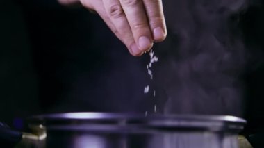 Man salt water boiling in a saucepan, dark background