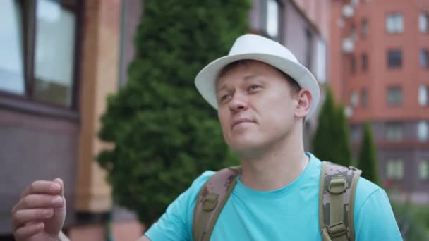 Joven con sombrero y mochila pasea por la ciudad, rastreando cámaras — Vídeos de Stock