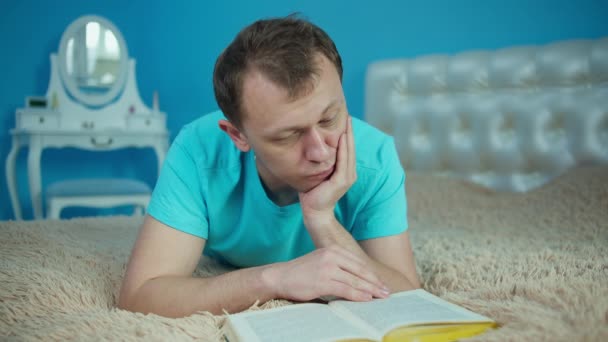 Młody atrakcyjny mężczyzna czytający książkę leżąc na łóżku — Wideo stockowe