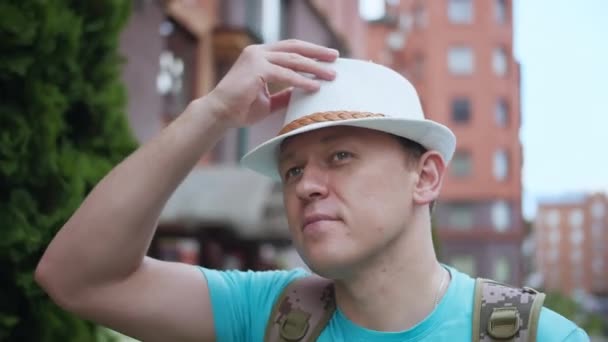 Joven con sombrero caminando por la ciudad, rastreando cámaras — Vídeo de stock