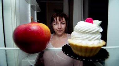 Geceleyin tombul genç bir kadın buzdolabından bir elma alır, diyet, uygun beslenme konsepti