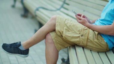 Bir turist elinde cep telefonuyla bir bankta oturur, kamera takibi yapar.