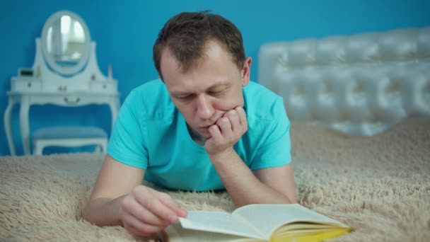 매력적 인 젊은 남자가 열려 있는 책을 침대에 놓고 누워 있다 — 비디오