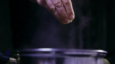 Tavadan buhar çıkıyor, adam tavaya baharat ekliyor, karanlık arka plan.