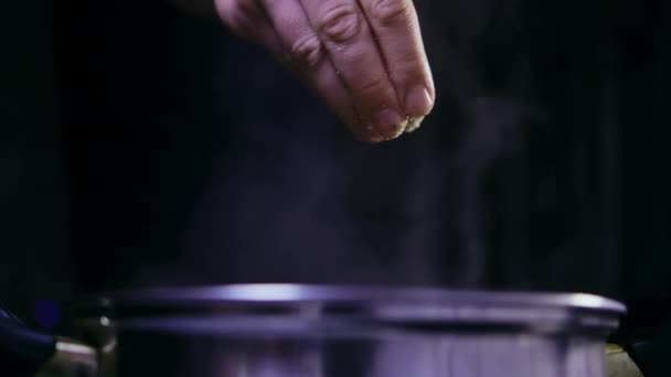 Парочка з каструлі, чоловік додає спеції на сковороду, темний фон — стокове відео