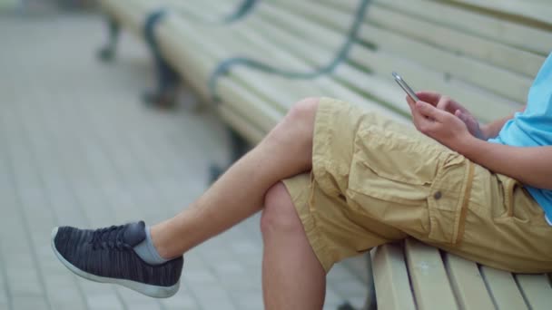 Turista senta-se com um telefone celular em suas mãos em um banco da cidade, rastreamento de câmera — Vídeo de Stock