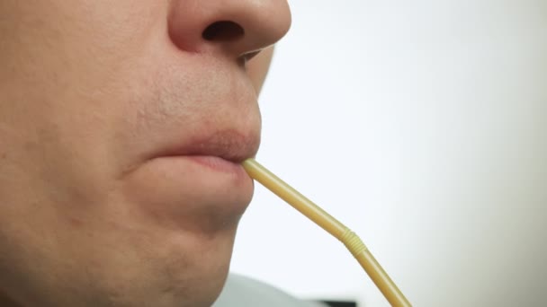 Close-up gezicht van jonge man drinken door middel van plastic cocktail tube, lichte achtergrond — Stockvideo